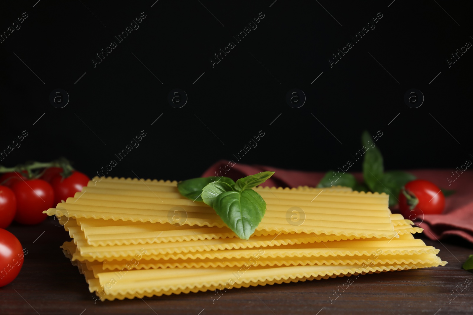 Photo of Uncooked lasagna sheets with cherry tomatoes and basil on wooden table