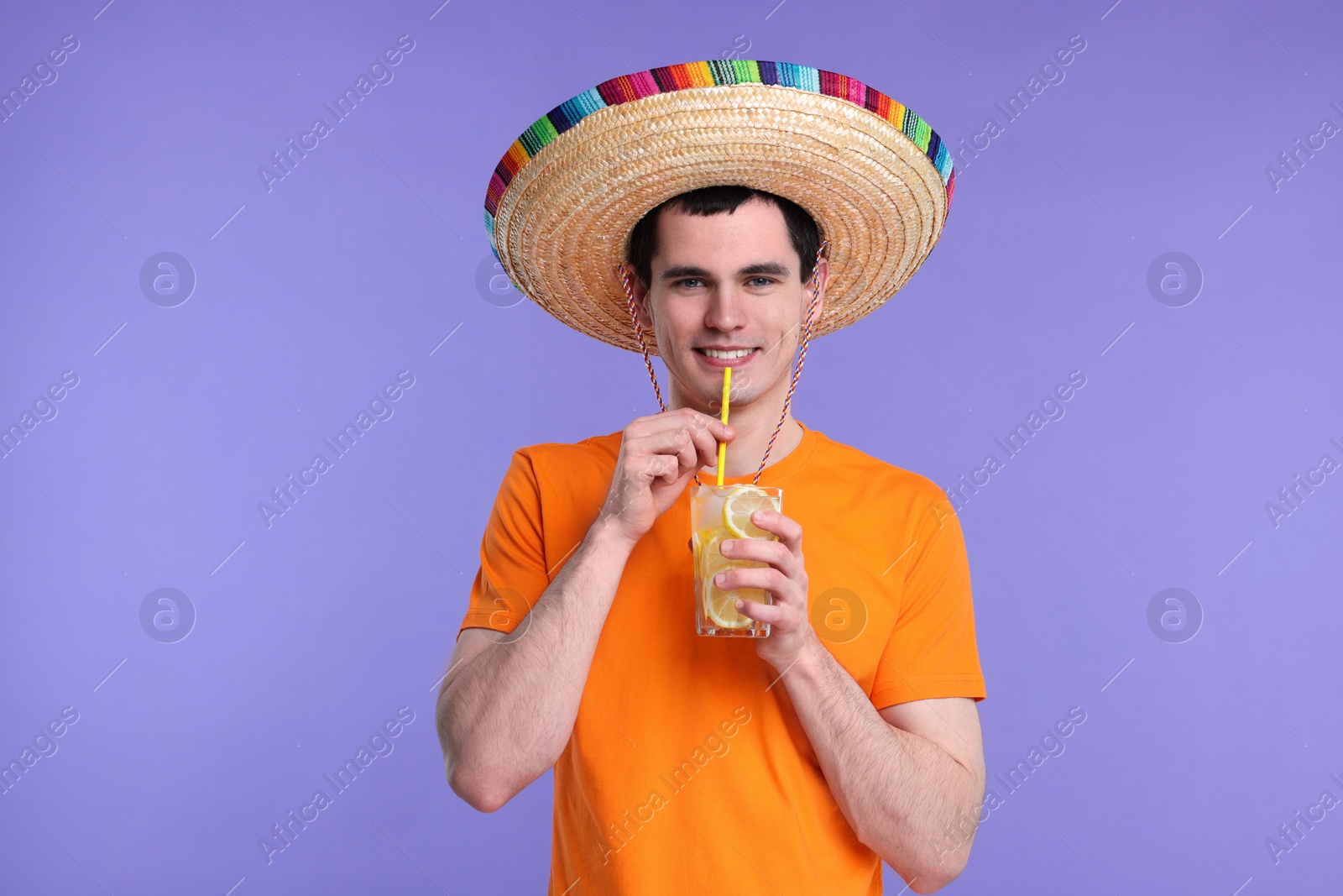 Photo of Young man in Mexican sombrero hat with cocktail on violet background