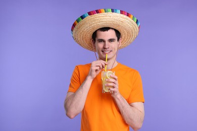 Young man in Mexican sombrero hat with cocktail on violet background