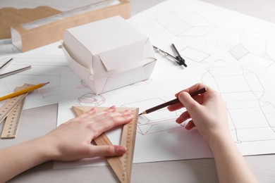 Photo of Woman creating packaging design at light wooden table, closeup