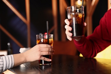 Photo of Young couple with glasses of refreshing cola at table indoors, closeup