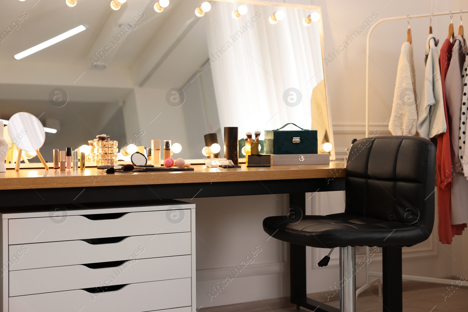 Photo of Makeup room. Stylish dressing table with mirror, chair and clothes rack