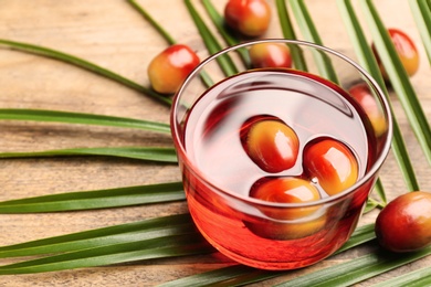 Palm oil in glass with fruits and tropical leaf on wooden table, closeup