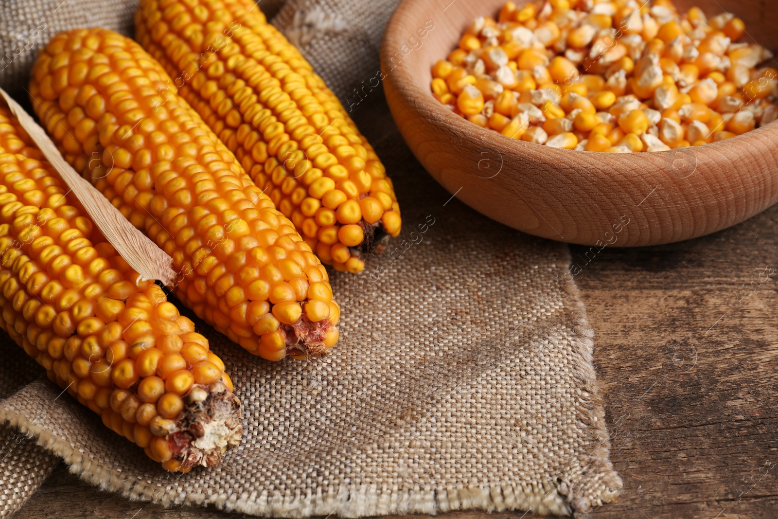 Photo of Delicious ripe corn cobs and bowl with seeds on wooden table