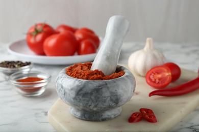 Photo of Red curry paste in mortar and ingredients on white marble table