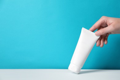 Photo of Woman with tube of hand cream at table against light blue background, closeup. Space for text