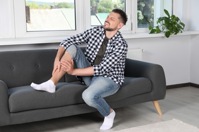 Man rubbing sore leg on sofa at home