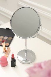 Photo of Mirror, cosmetic products and pink roses on white dressing table, closeup