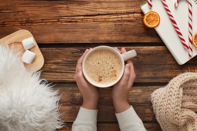 Photo of Woman with cup of coffee at wooden table, top view. Cozy winter