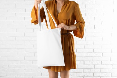 Woman with white textile bag near brick wall, closeup. Space for design