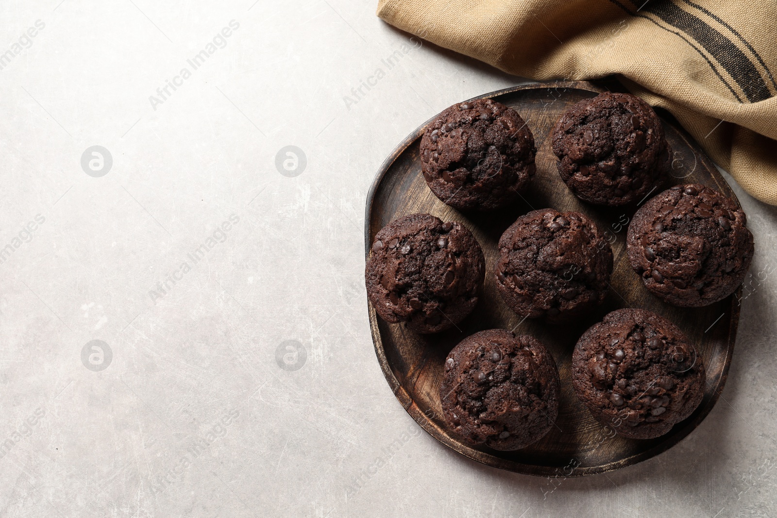 Photo of Board with delicious chocolate muffins on light table, top view. Space for text