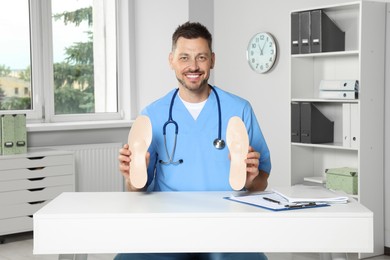 Photo of Handsome male orthopedist showing insoles in hospital