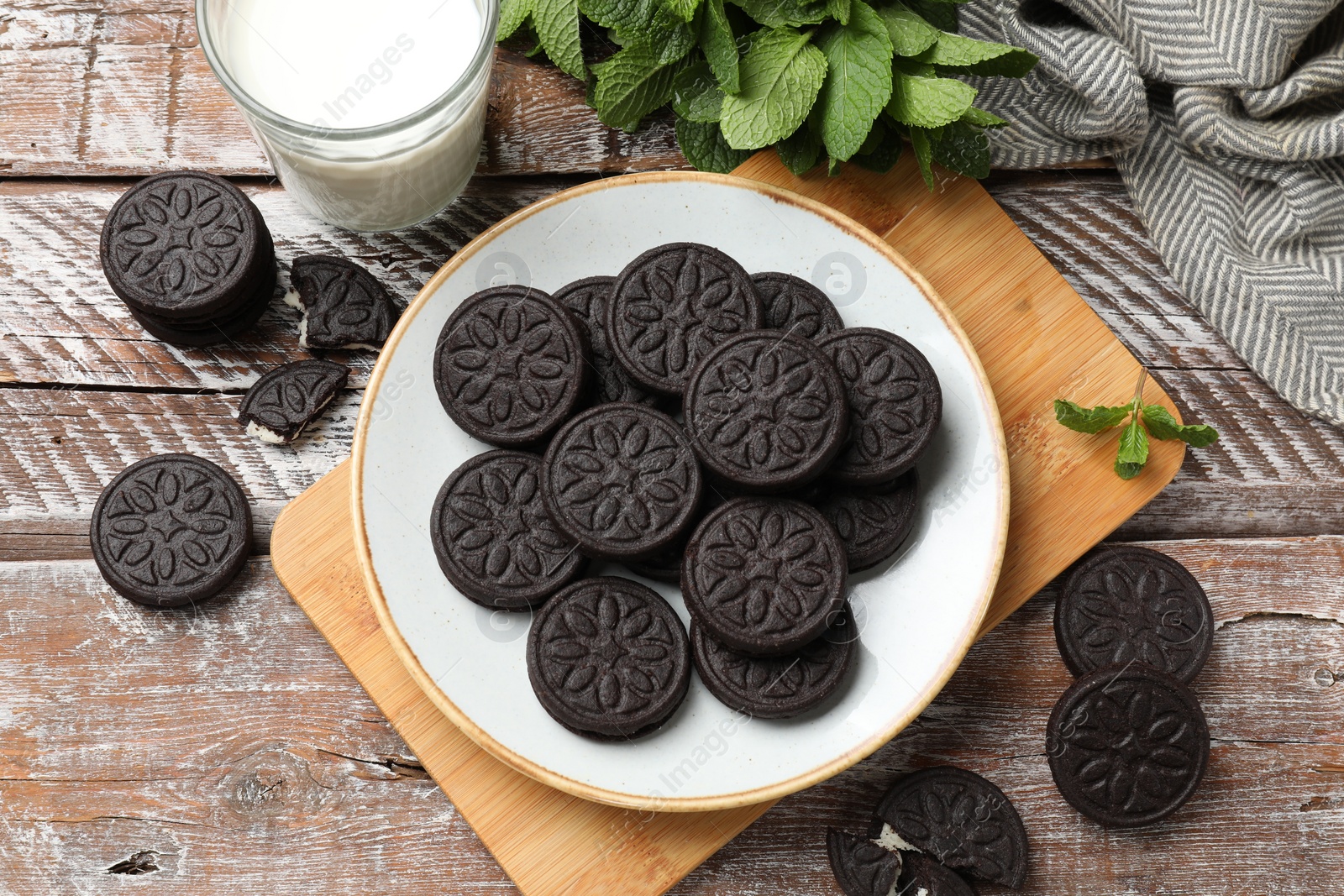 Photo of Plate with tasty sandwich cookies, mint and milk on wooden rustic table, flat lay