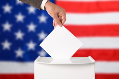 Image of Election in USA. Man putting his vote into ballot box against national flag of United States, closeup