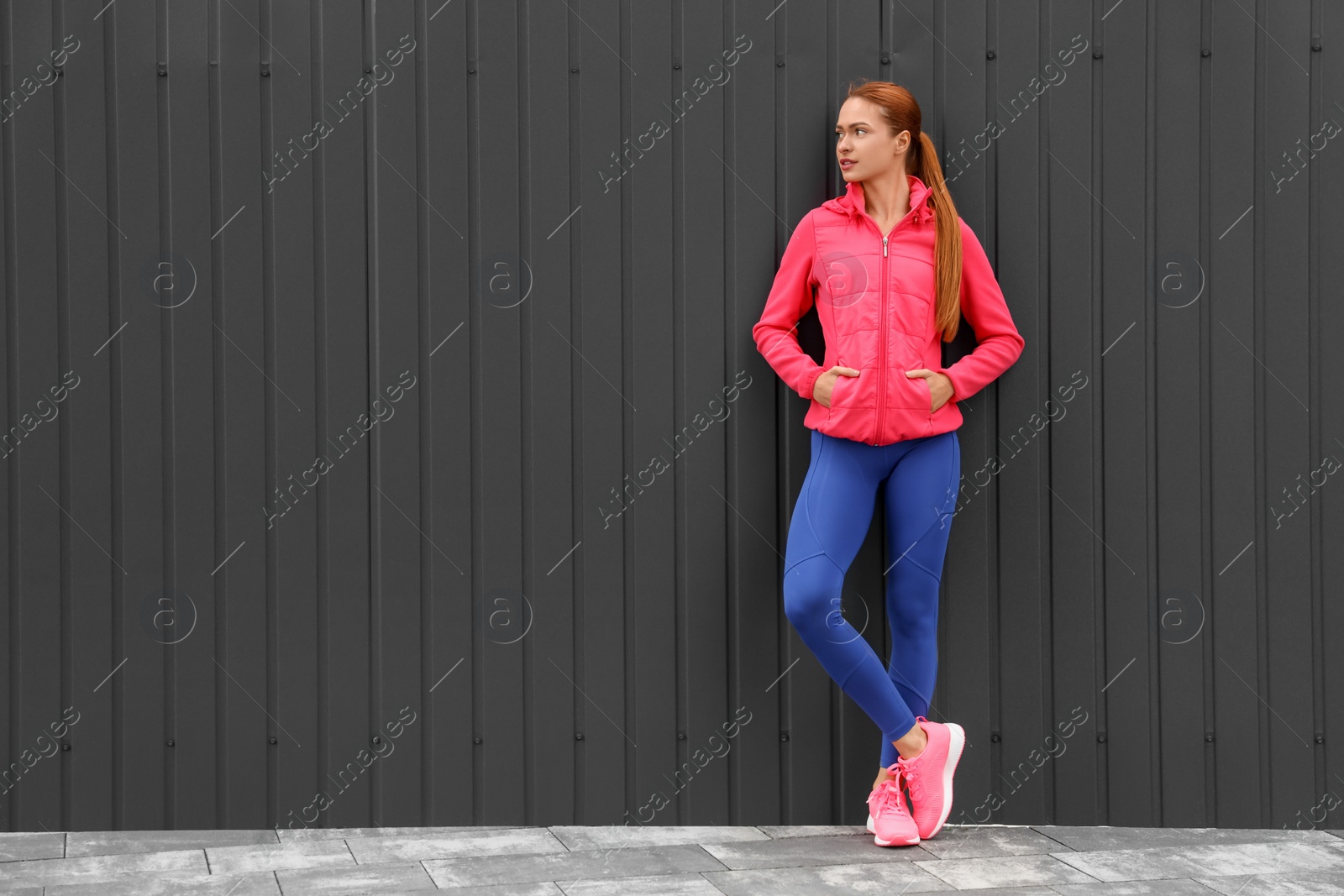 Photo of Beautiful woman in gym clothes near dark grey wall on street, space for text