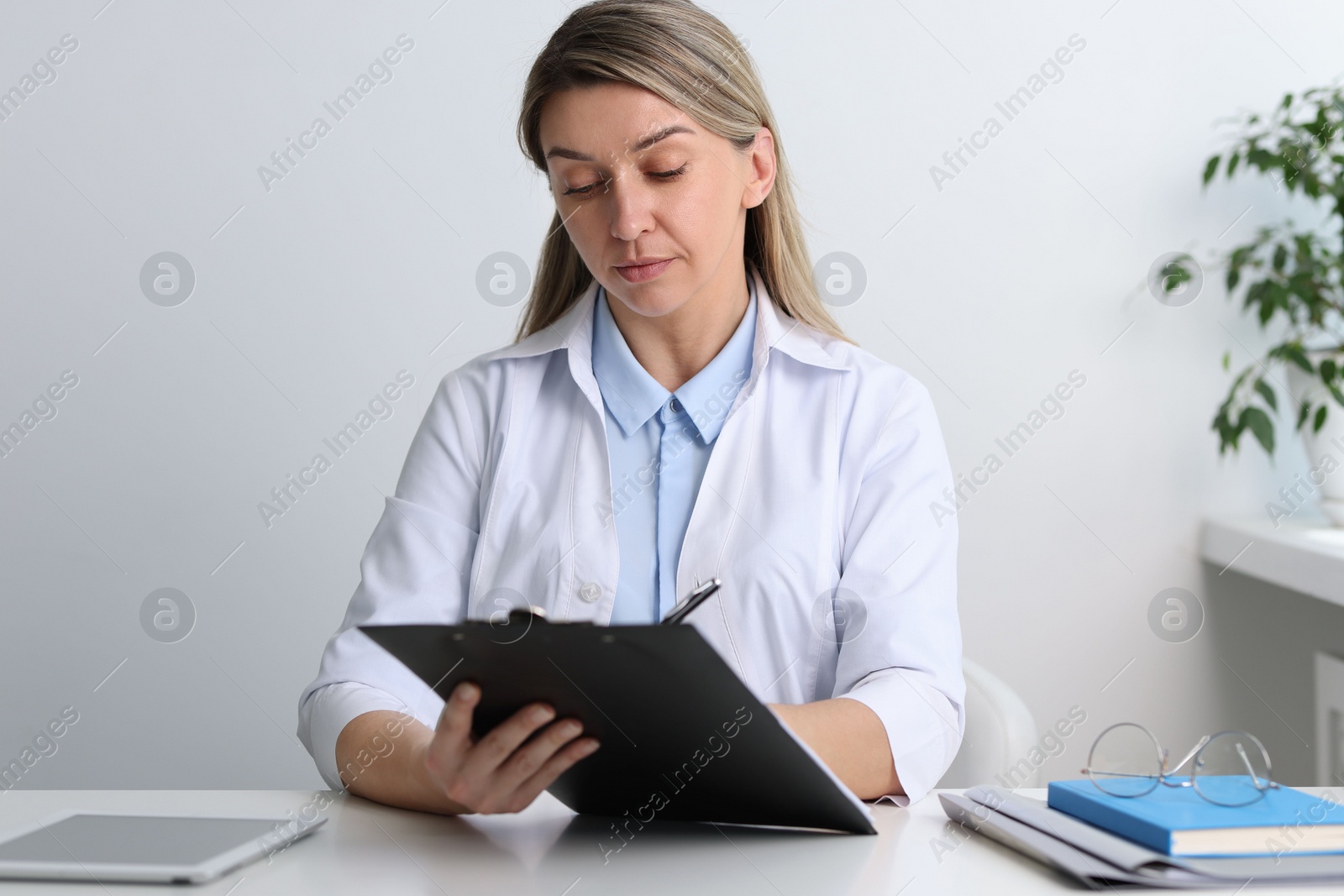 Photo of Portrait of happy doctor with clipboard at white table in hospital