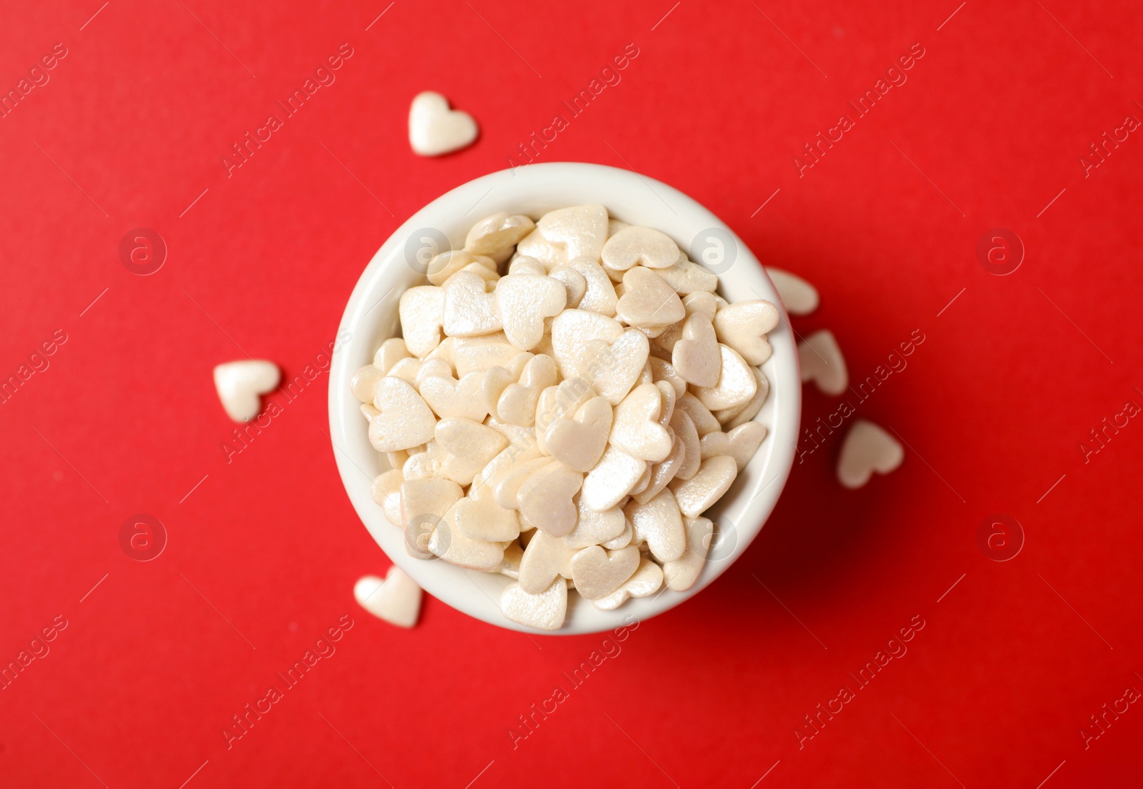 Photo of White heart shaped sprinkles and bowl on red background, flat lay