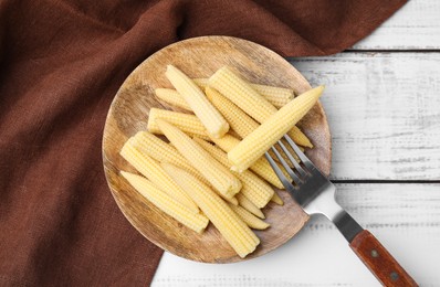 Photo of Pickled baby corn and fork on white wooden table, top view