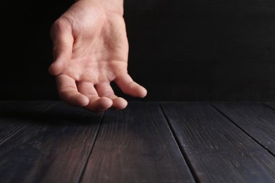 Photo of Man holding hand above black wooden table, closeup. Space for text