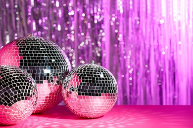 Photo of Many shiny disco balls on table against blurred background, toned in pink. Space for text