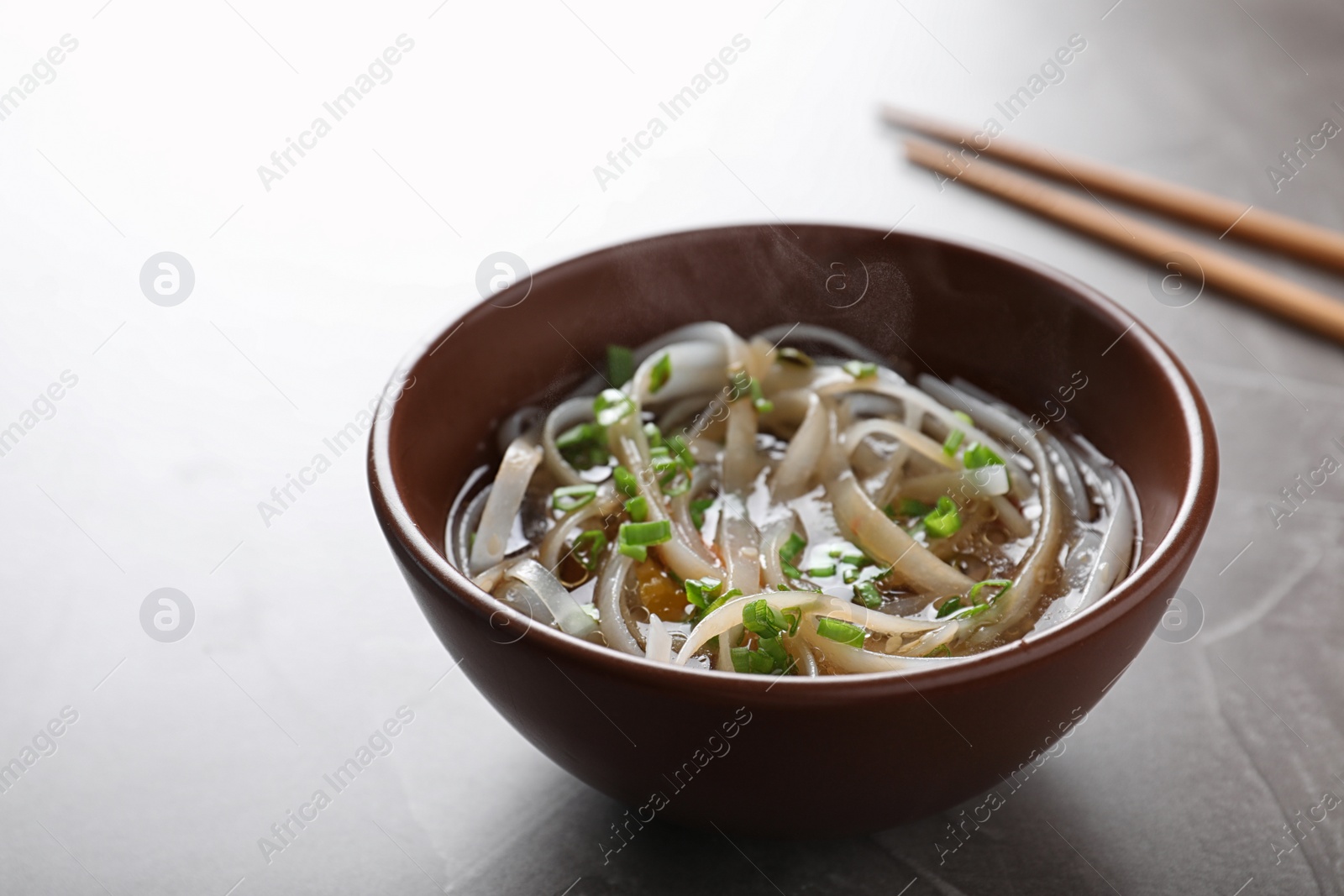 Photo of Bowl of delicious rice noodles with broth and herb on table
