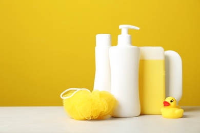 Photo of Baby cosmetic products, toy and accessories on white table against yellow background. Space for text