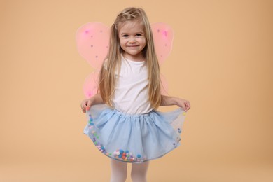 Photo of Cute little girl in fairy costume with pink wings on beige background