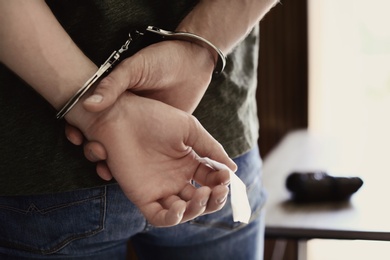 Man detained in handcuffs holding bag with drug indoors, closeup. Criminal law