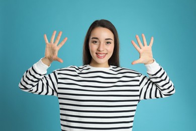 Photo of Woman showing number ten with her hands on light blue background