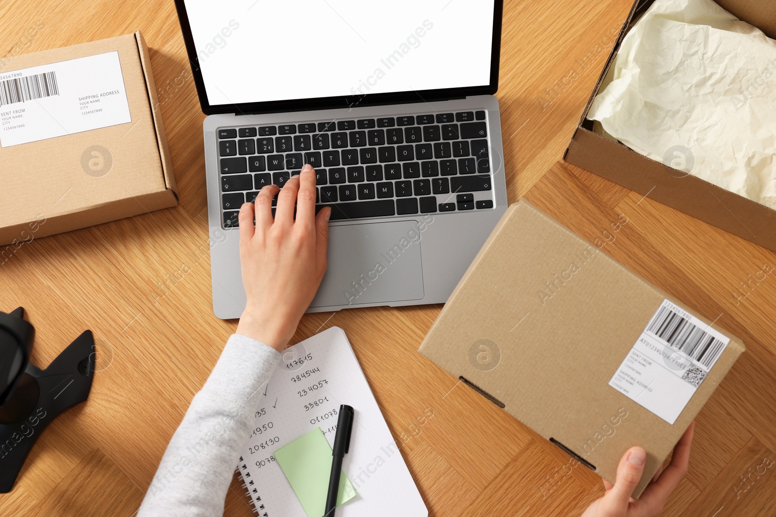 Photo of Woman with laptop and parcel working at wooden table, top view. Online store