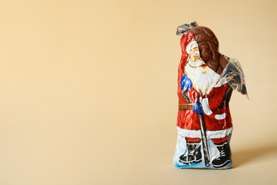 Photo of Sweet chocolate Santa Claus candy in slightly open foil wrapper on beige background, space for text