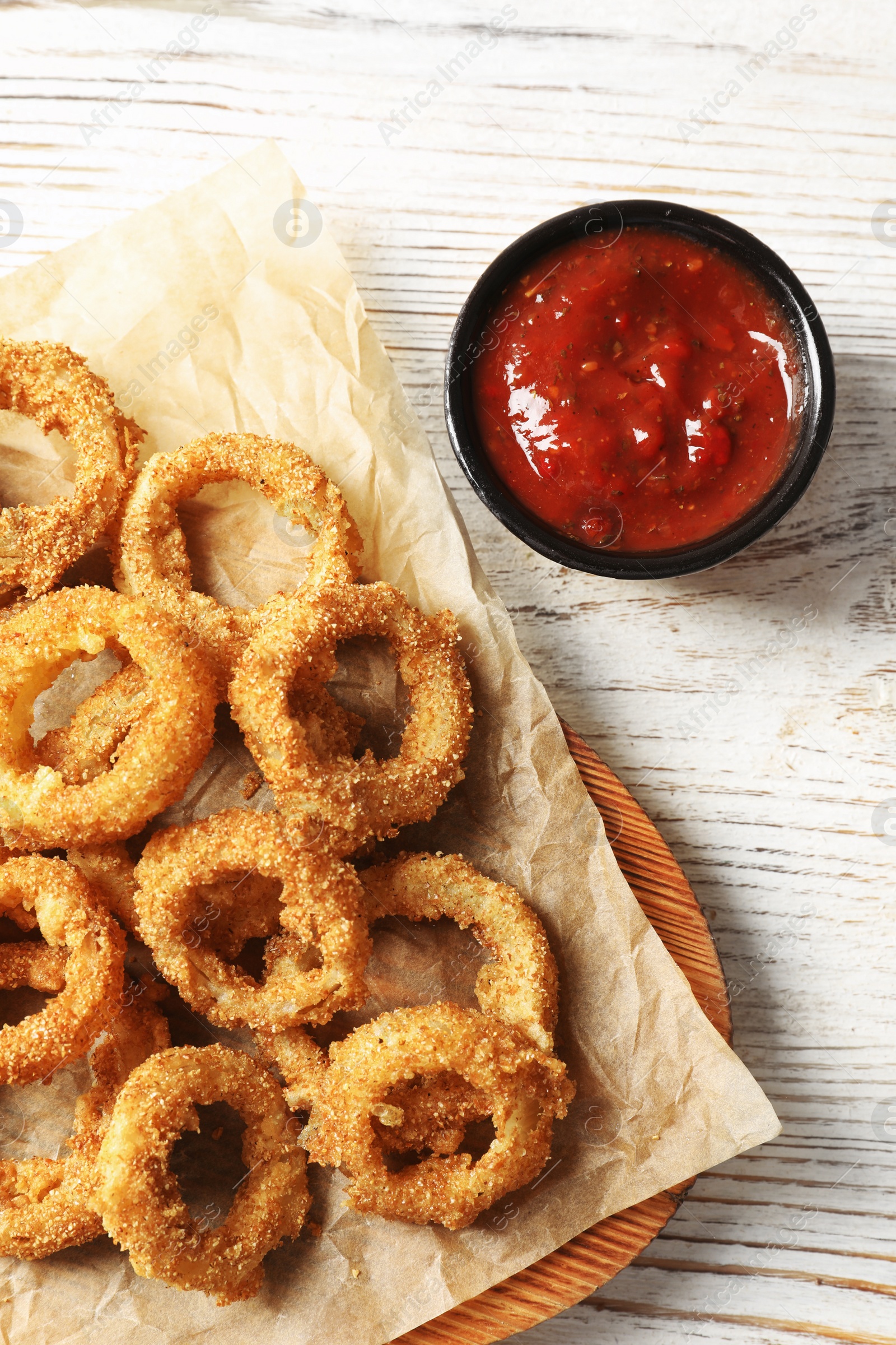 Photo of Homemade crunchy fried onion rings with tomato sauce on wooden table, top view