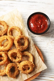 Photo of Homemade crunchy fried onion rings with tomato sauce on wooden table, top view