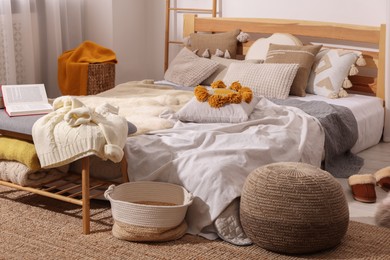 Large comfortable bed with soft pillows, blankets, clothes and slippers in room. Home textile