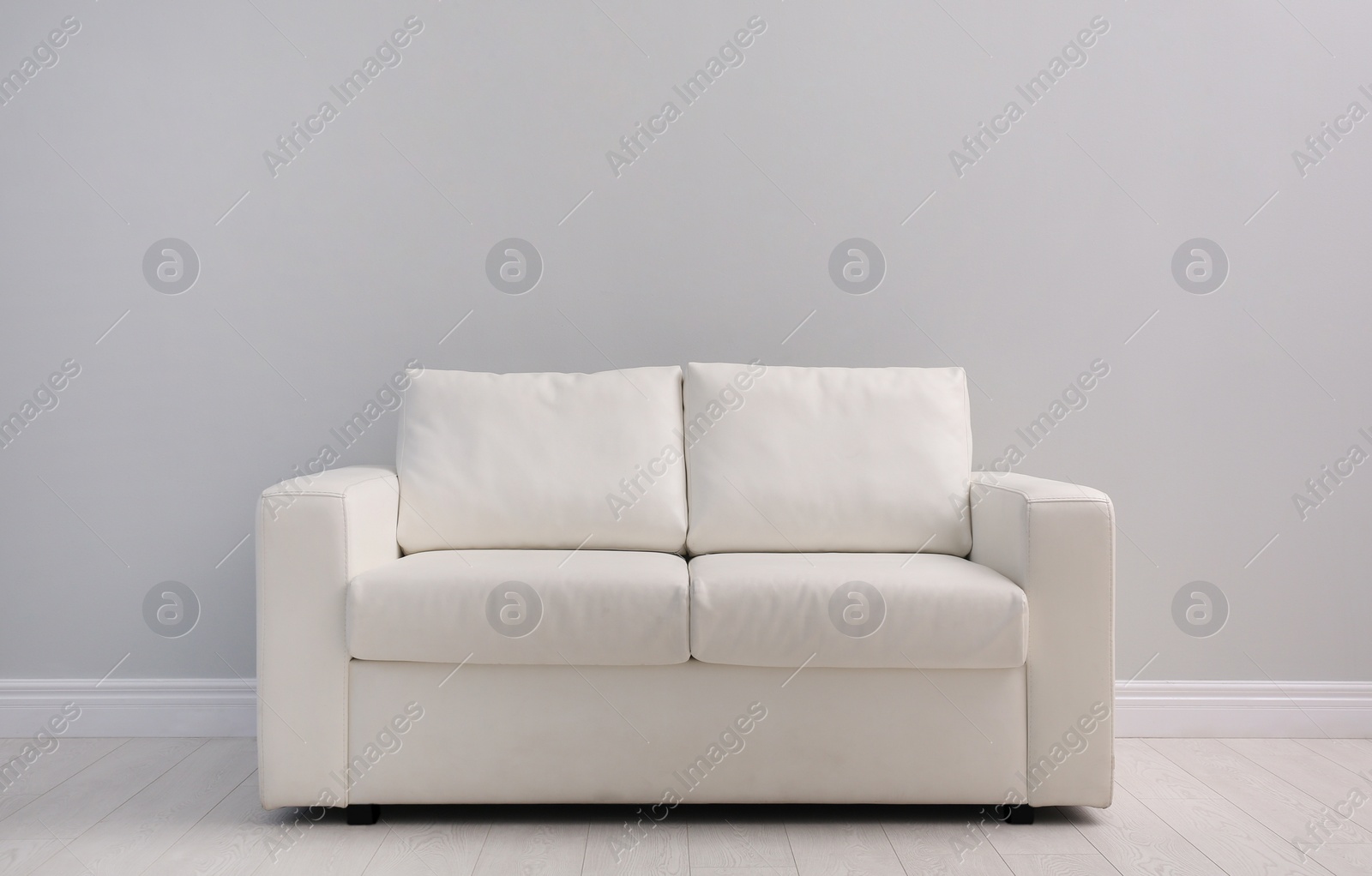 Photo of Comfortable white sofa near light wall indoors, space for text. Simple interior