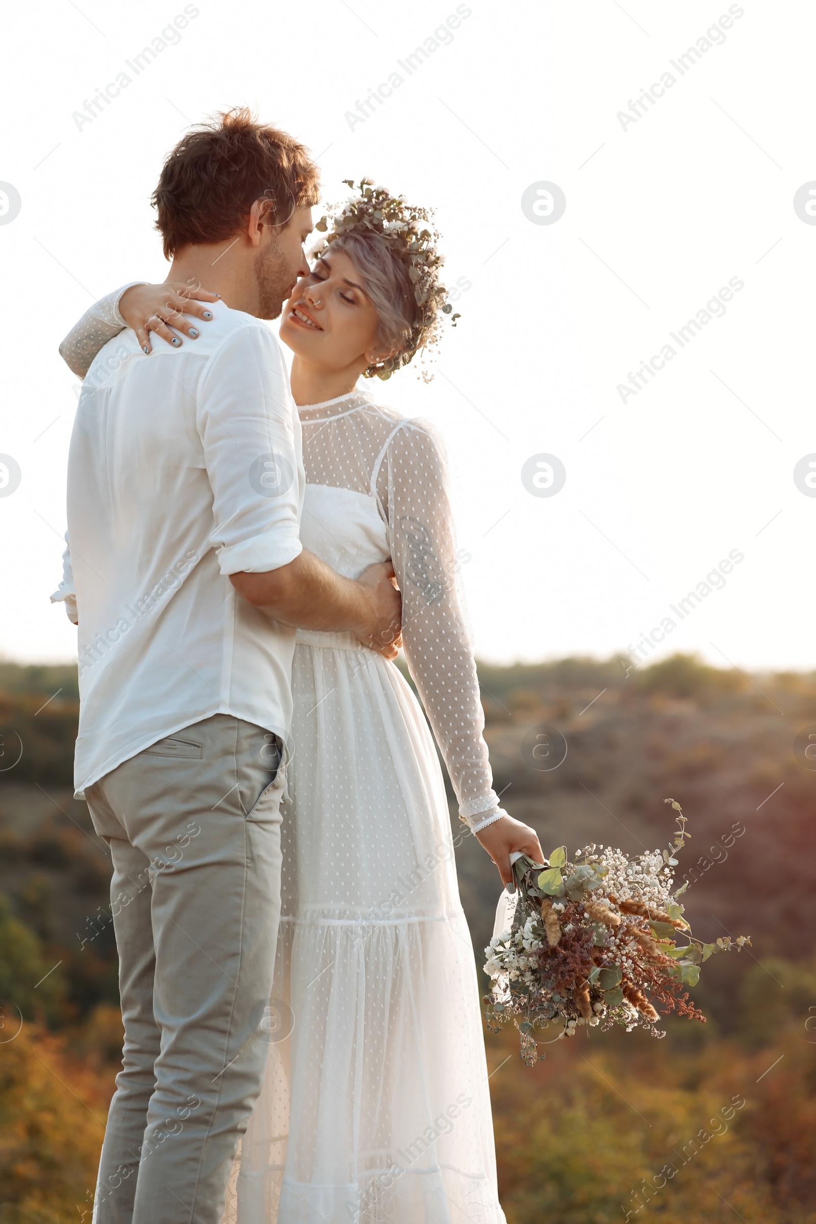 Photo of Happy newlyweds with beautiful field bouquet outdoors