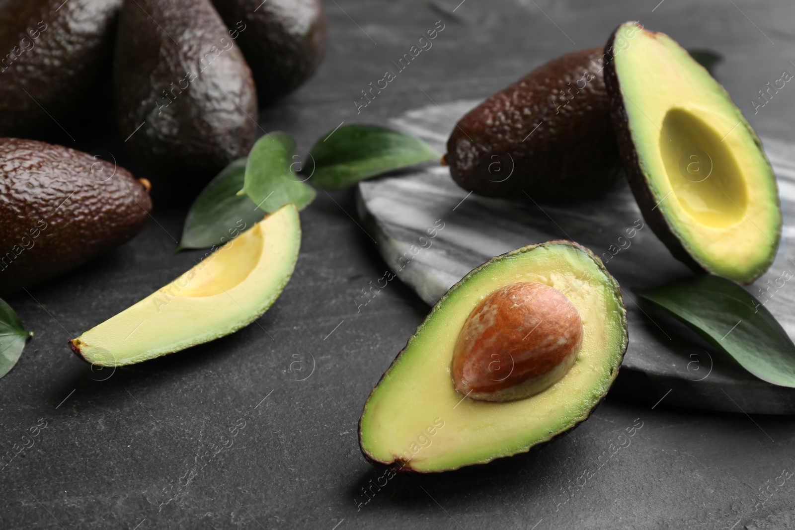 Photo of Whole and cut avocados with green leaves on black table