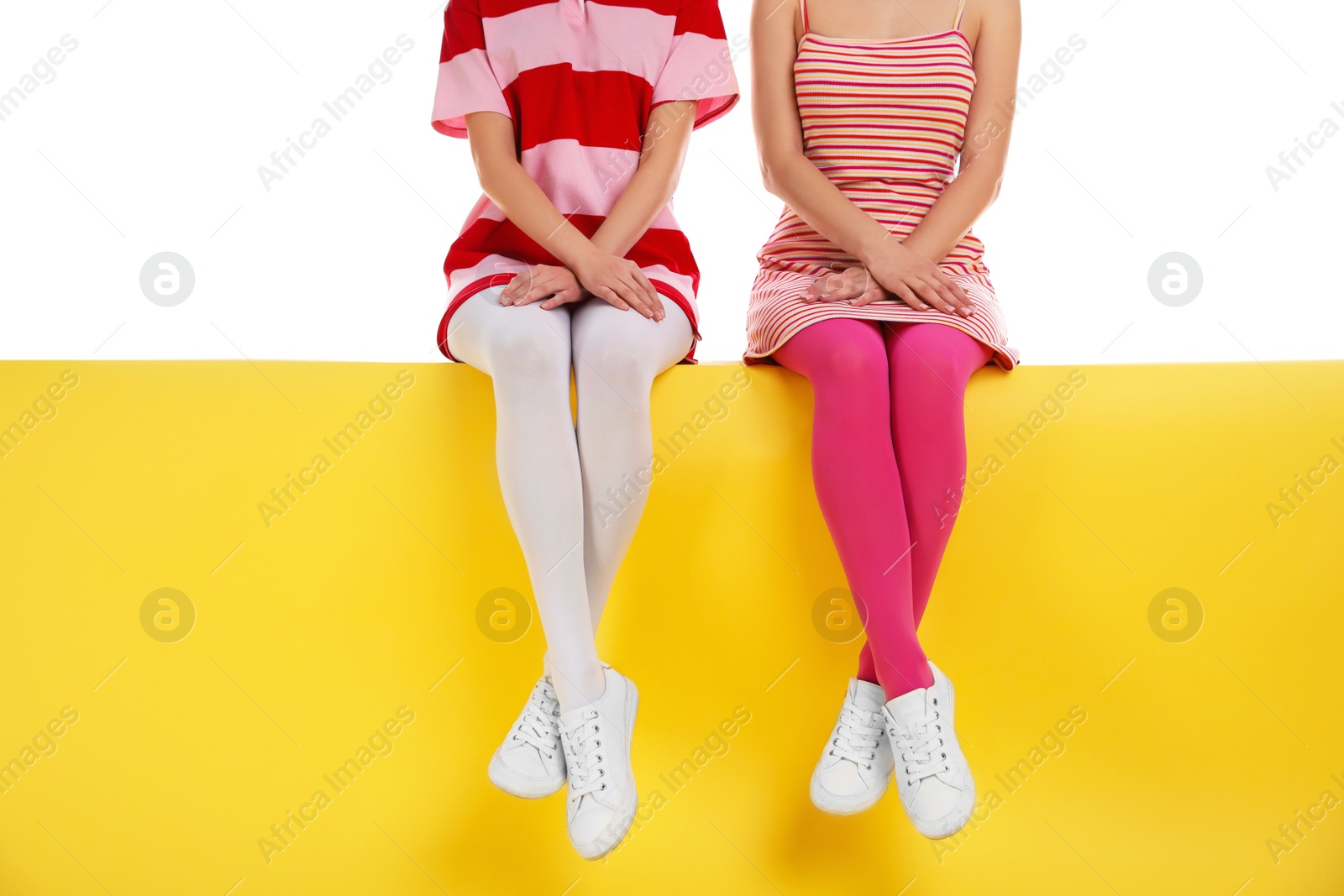 Photo of Women wearing bright tights sitting on color background, closeup