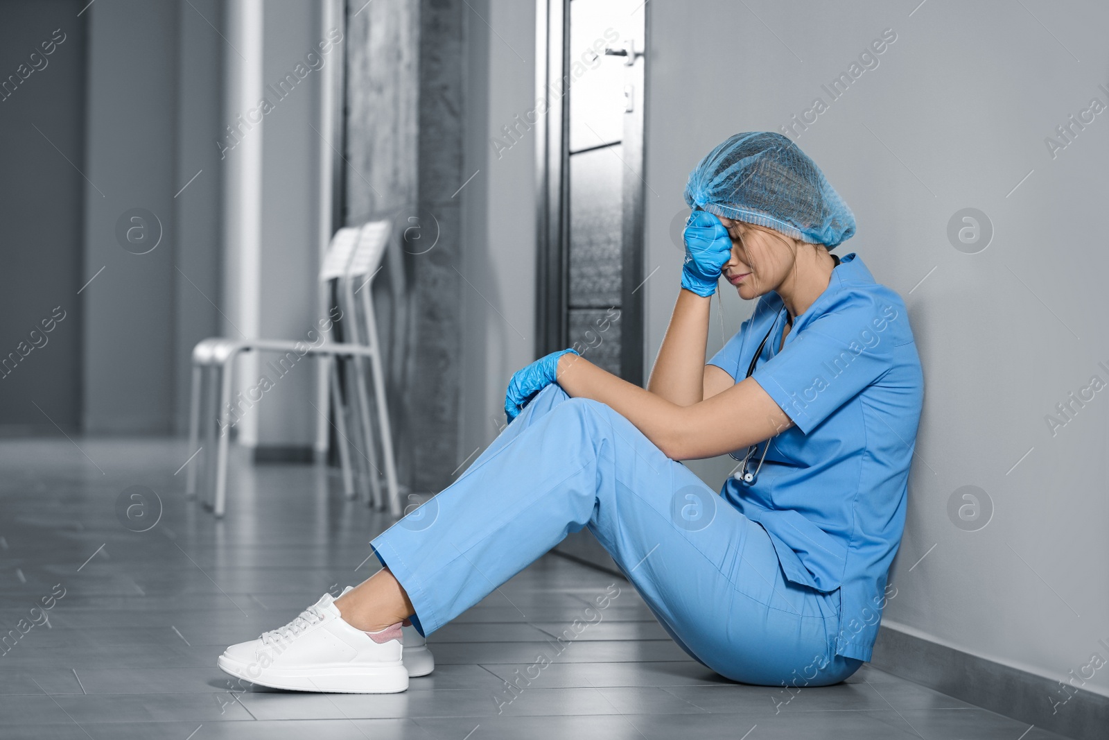 Photo of Exhausted doctor sitting on floor in hospital, space for text