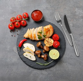 Photo of Fried chicken breasts served with sauce and garnish on grey background, top view