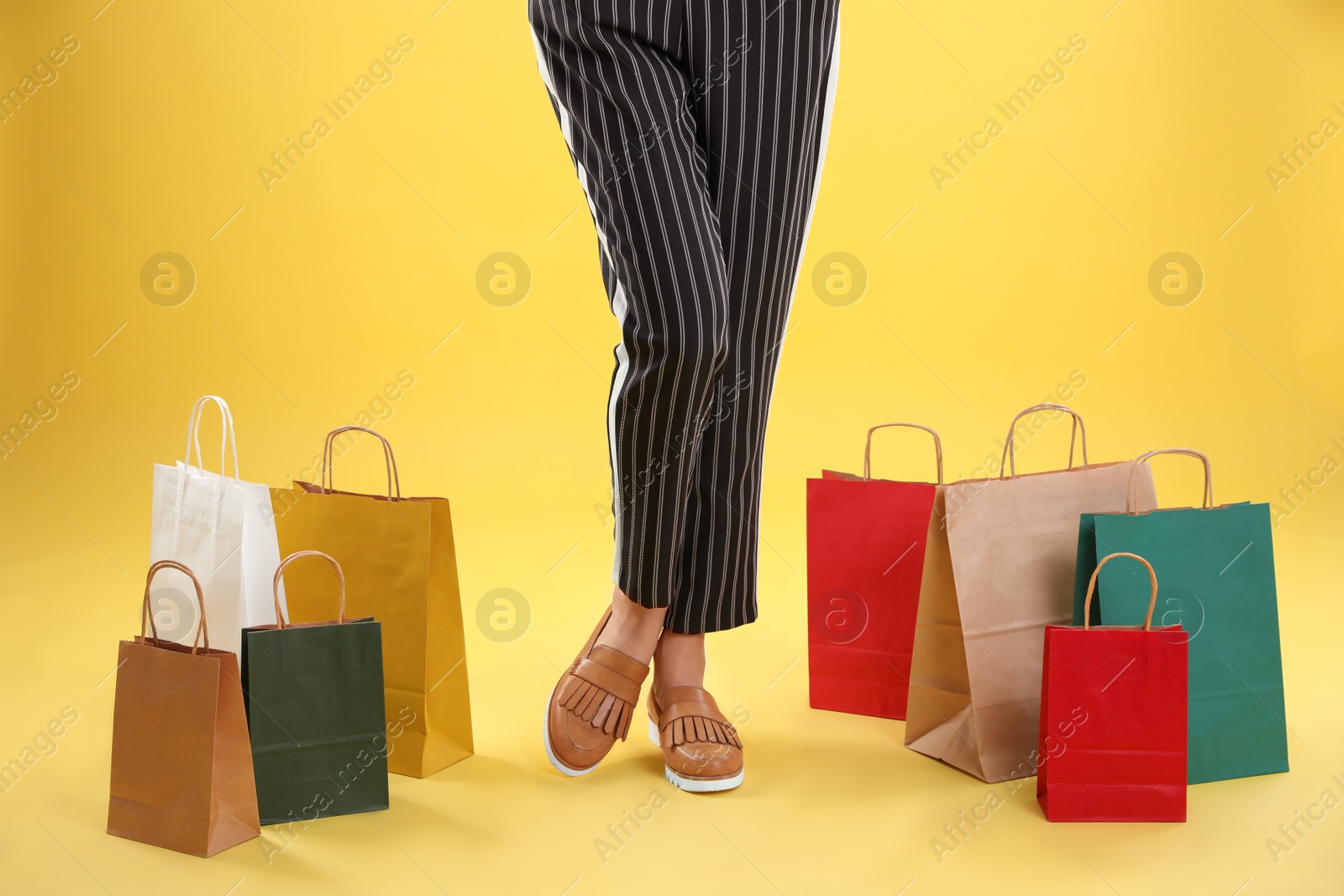 Photo of Young woman with shopping bags on color background, closeup of legs