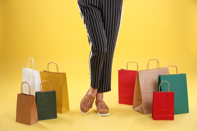 Young woman with shopping bags on color background, closeup of legs