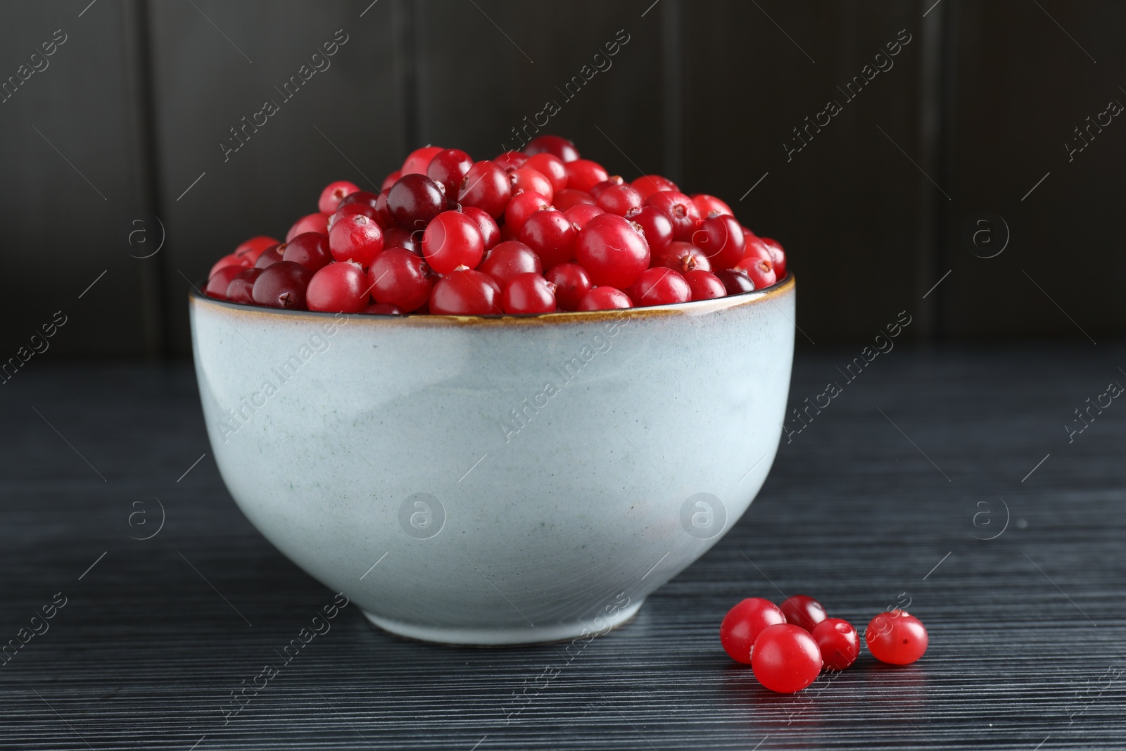 Photo of Cranberries in bowl on black wooden table, closeup