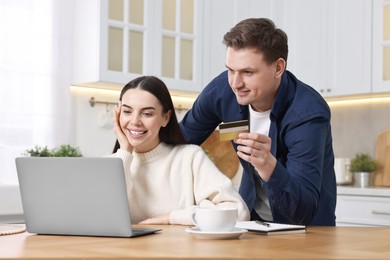 Happy couple with laptop and credit card shopping online in kitchen