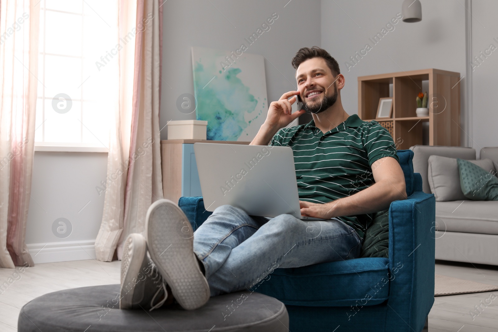 Photo of Young man working with laptop on armchair in home office