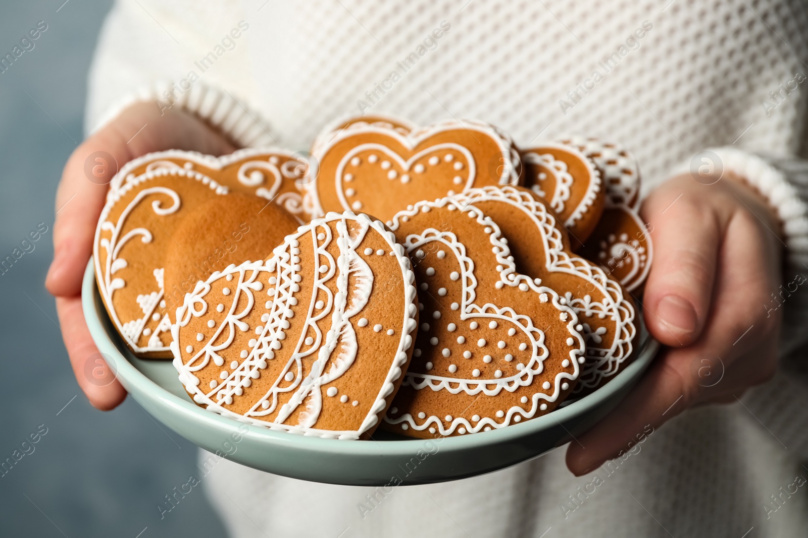 Photo of Woman holding plate with tasty heart shaped gingerbread cookies, closeup