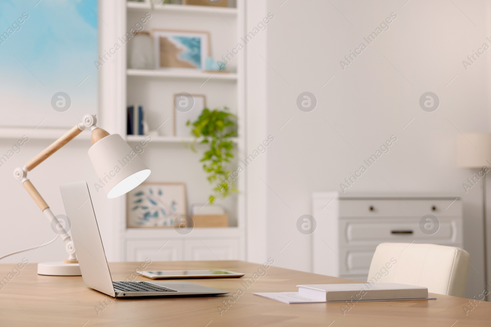 Photo of Interior design. Cosy workplace with laptop and lamp on wooden table. Space for text