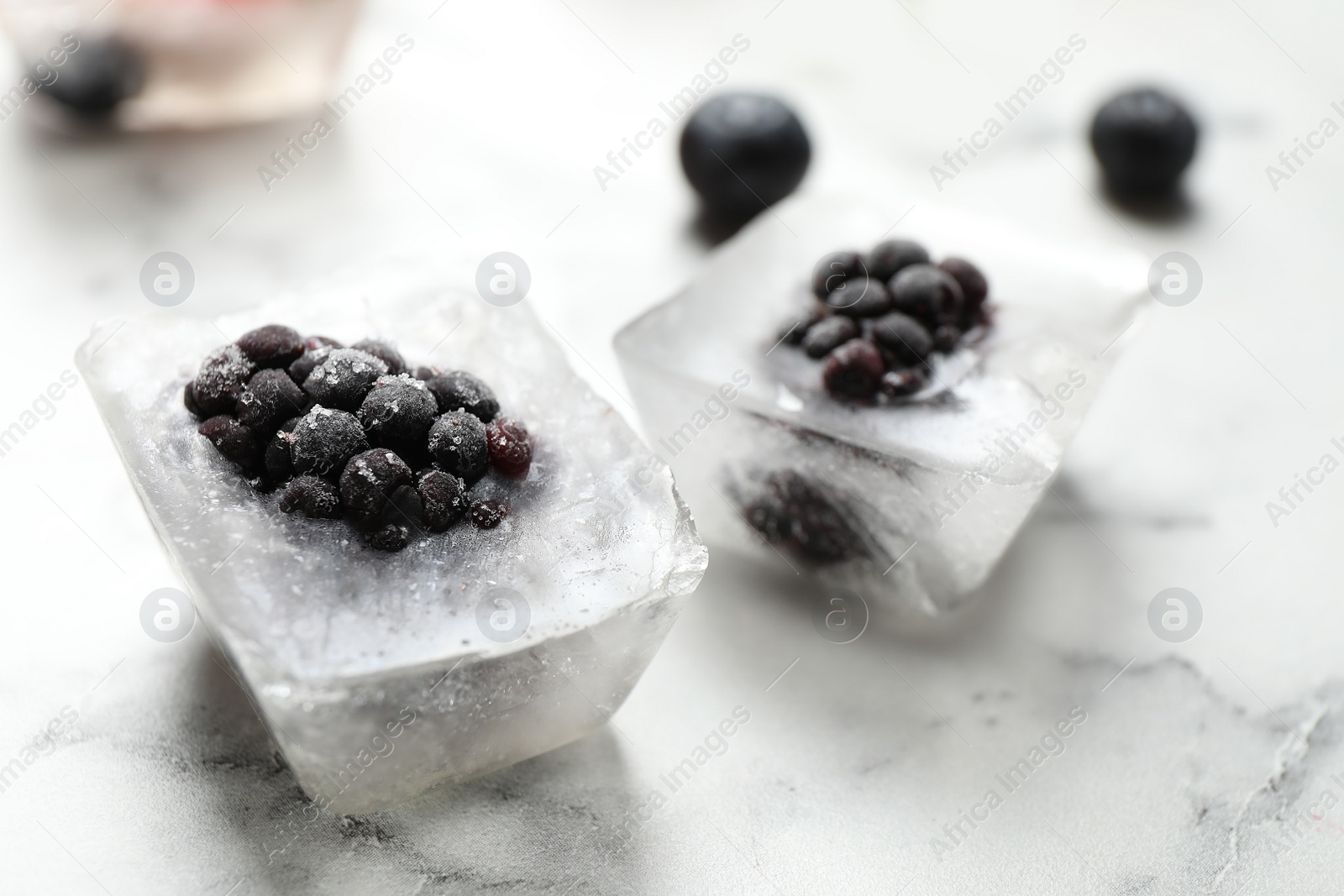 Photo of Ice cubes with blackberries on white marble table, closeup