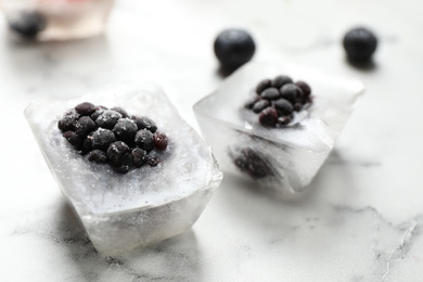 Ice cubes with blackberries on white marble table, closeup