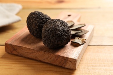 Photo of Black truffles with board on wooden table, closeup